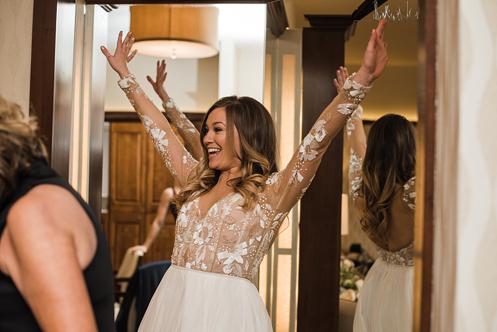 Bride cheers with arms in the air after she puts her wedding dress on