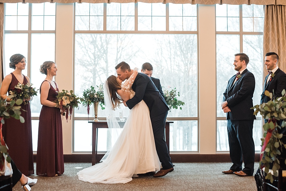Bride and groom share first kiss during indoor winter ceremony at Scioto Reserve Country Club in Powell, Ohio