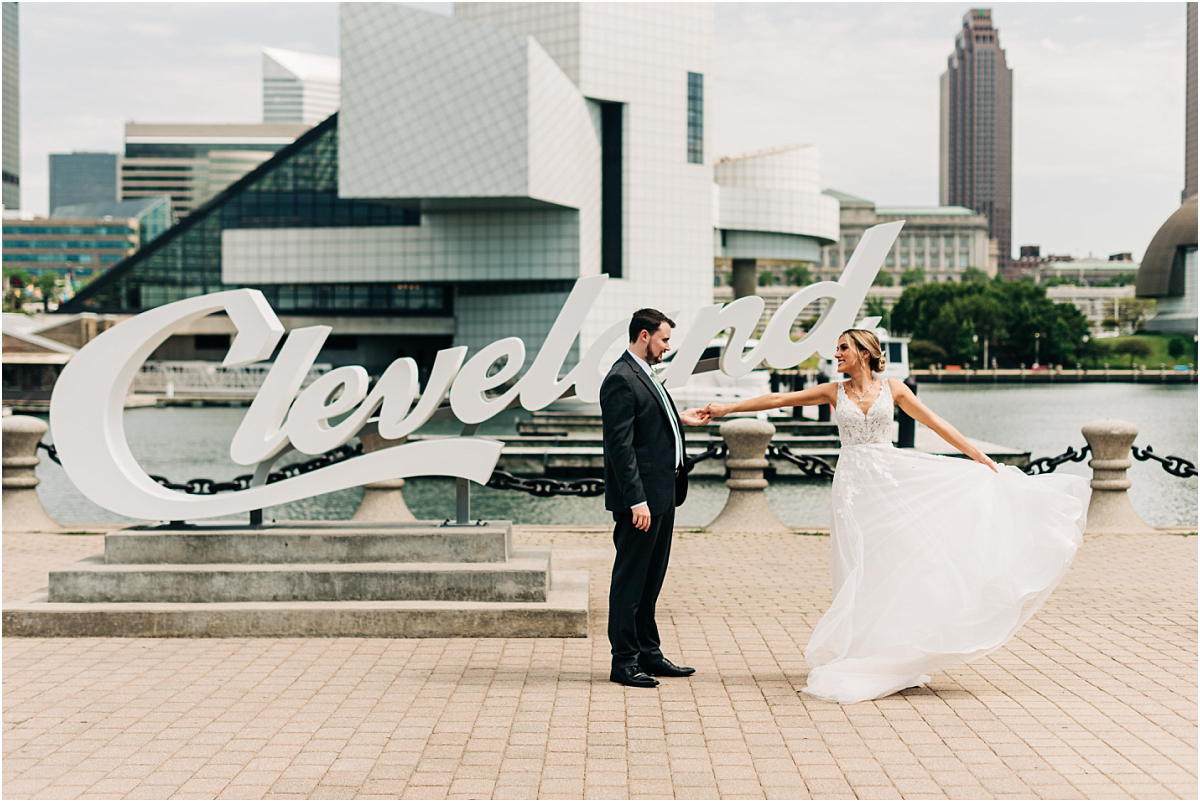 groom twirls bride in front of cleveland sign