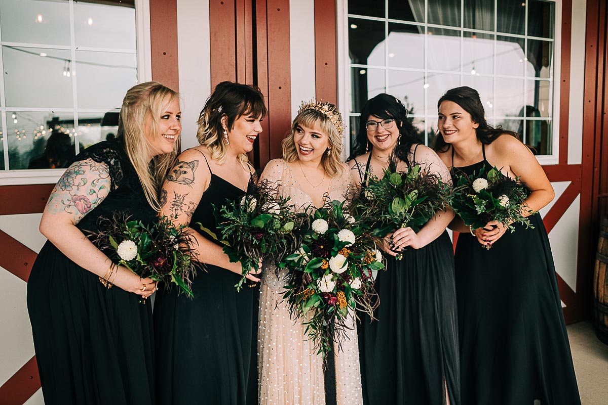 bride and bridesmaids giggle in front of the Barn at Blystone Farm
