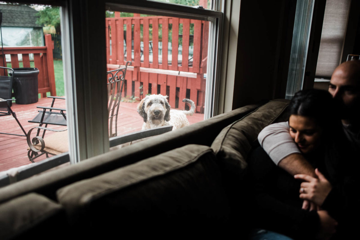Engaged couples dog looks at them through the window during their engagement session