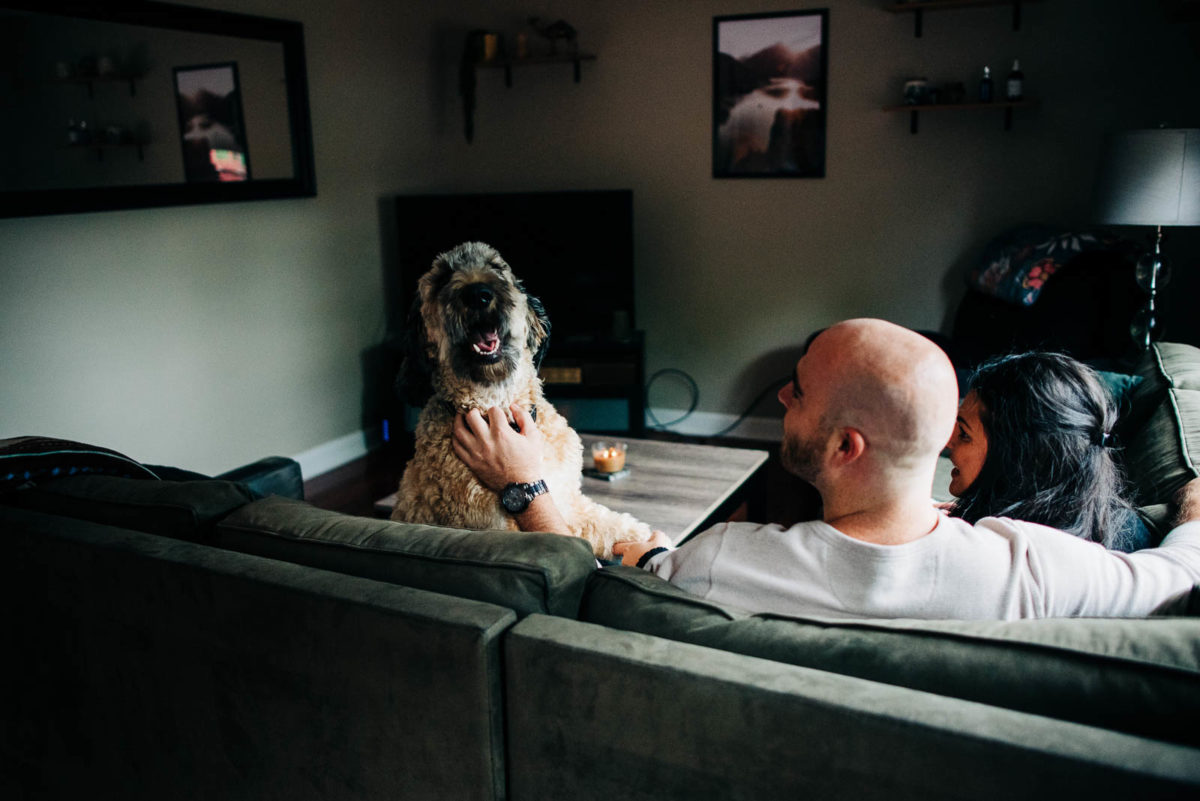 Groom to be scratches his dogs neck after letting him join their moody engagement session