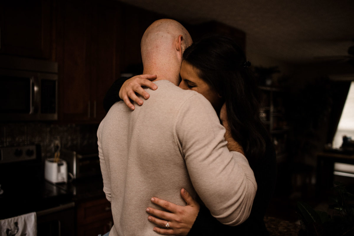 Engaged couple snuggles closely on the kitchen counter during their engagement session