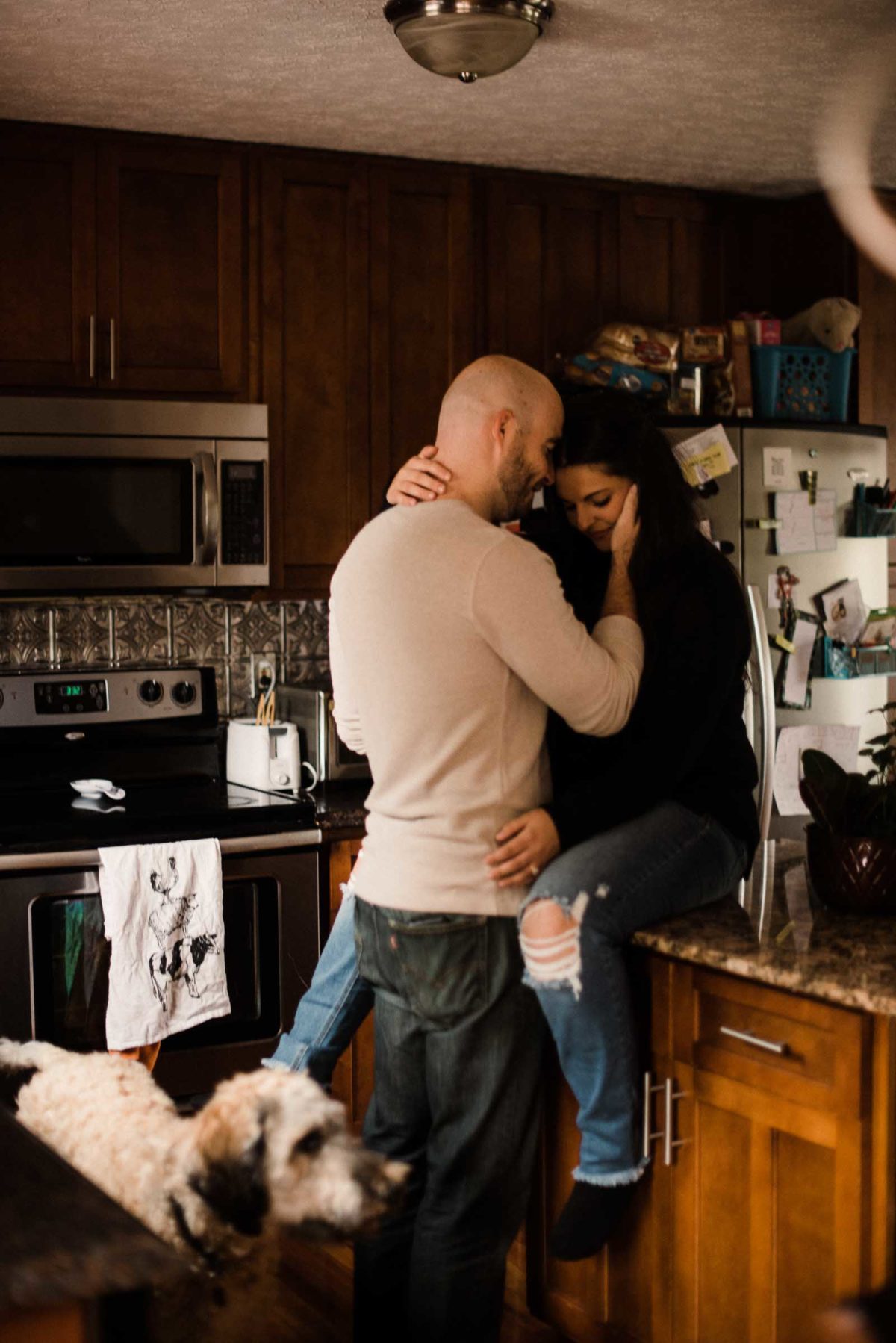 Engaged couple snuggles closely on the kitchen counter during their engagement session