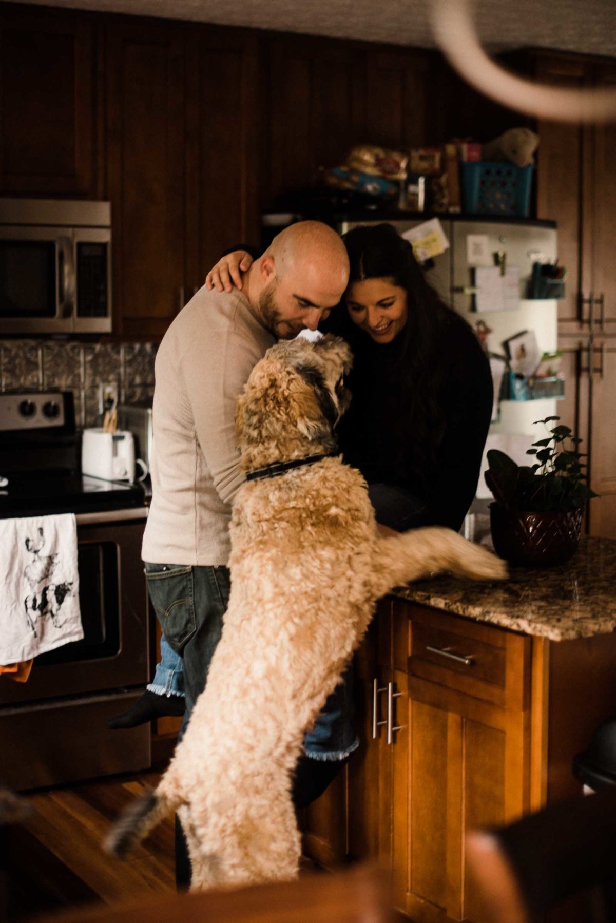 Engaged couple plays in their kitchen with their dog