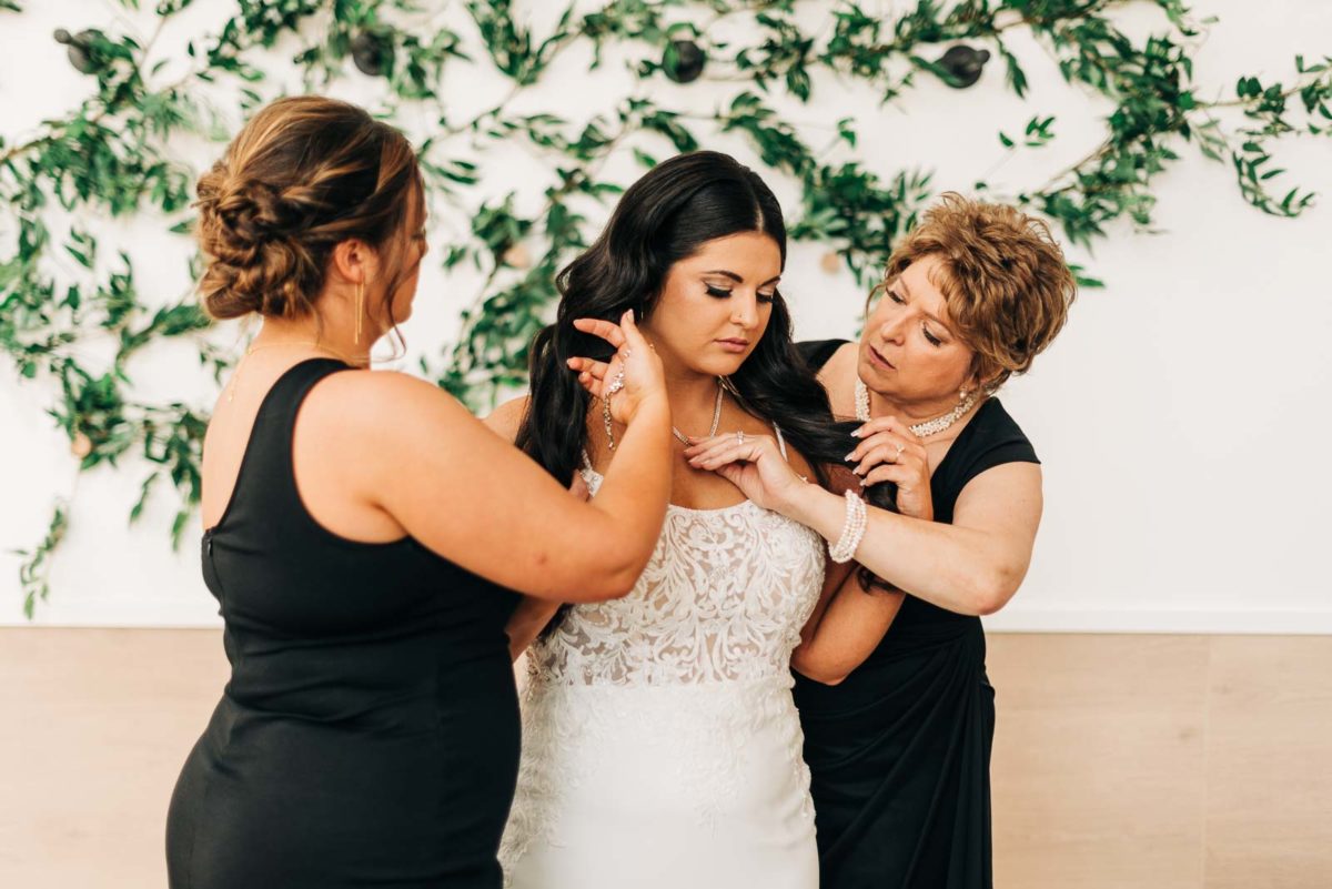 Brides mom and sister help her get dressed in the bridal suite at Retreat 21