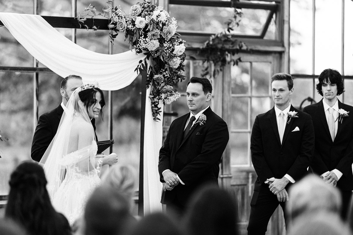 Groom watches his bride during their vow exchange at Oak Grove