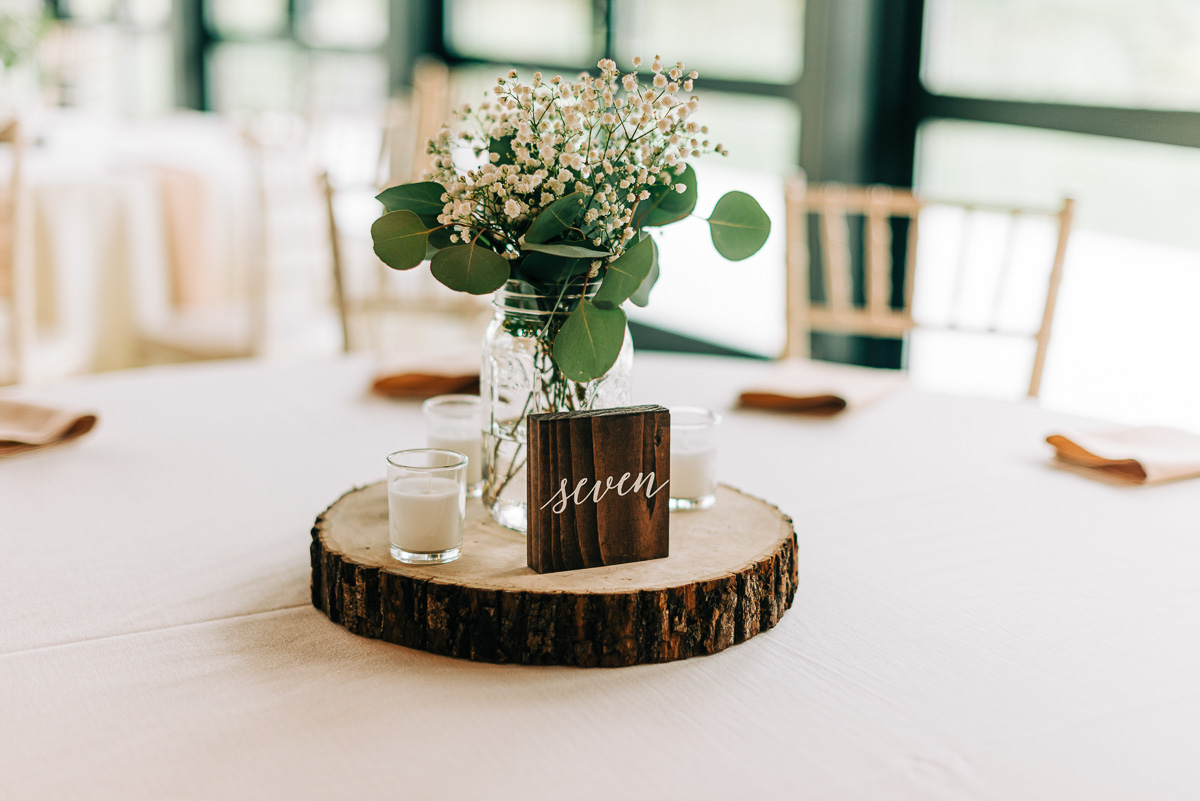 Babies breath in a mason jar, candles and a wooden block featuring a table number