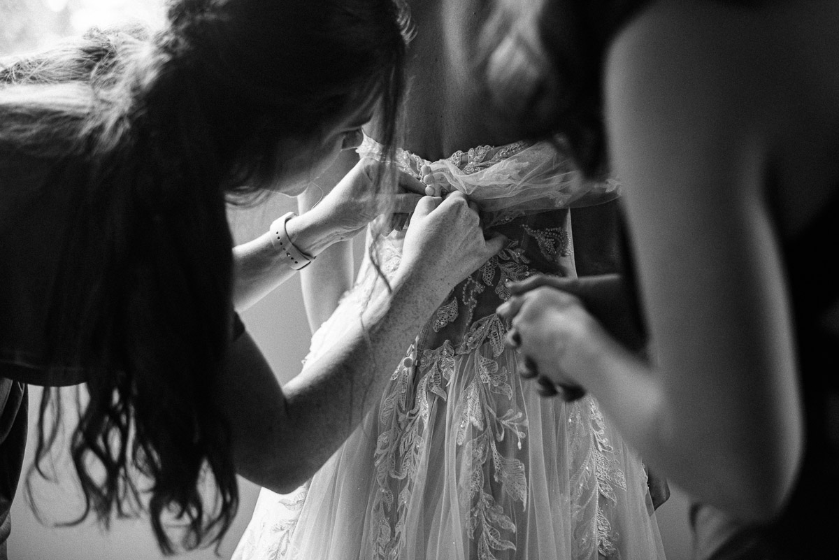 Bridesmaids button the Bride into her dress at Oak Grove