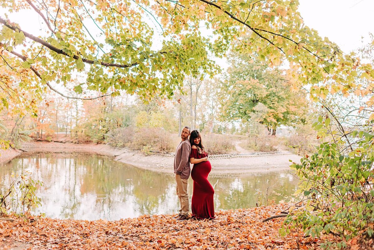 Maternity photographer poses couple back to back in front of Hoover Reservoir in Westerville, Ohio.