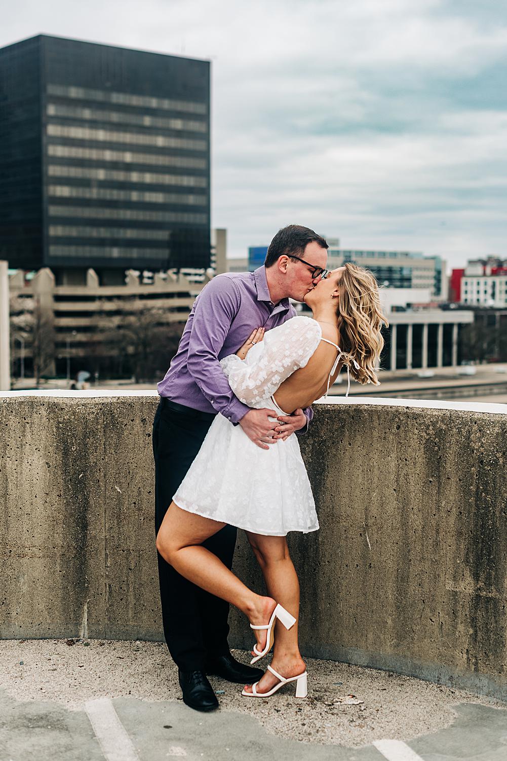 Newly engaged couple embrace in a kiss on top of a parking garage in Downtown Columbus