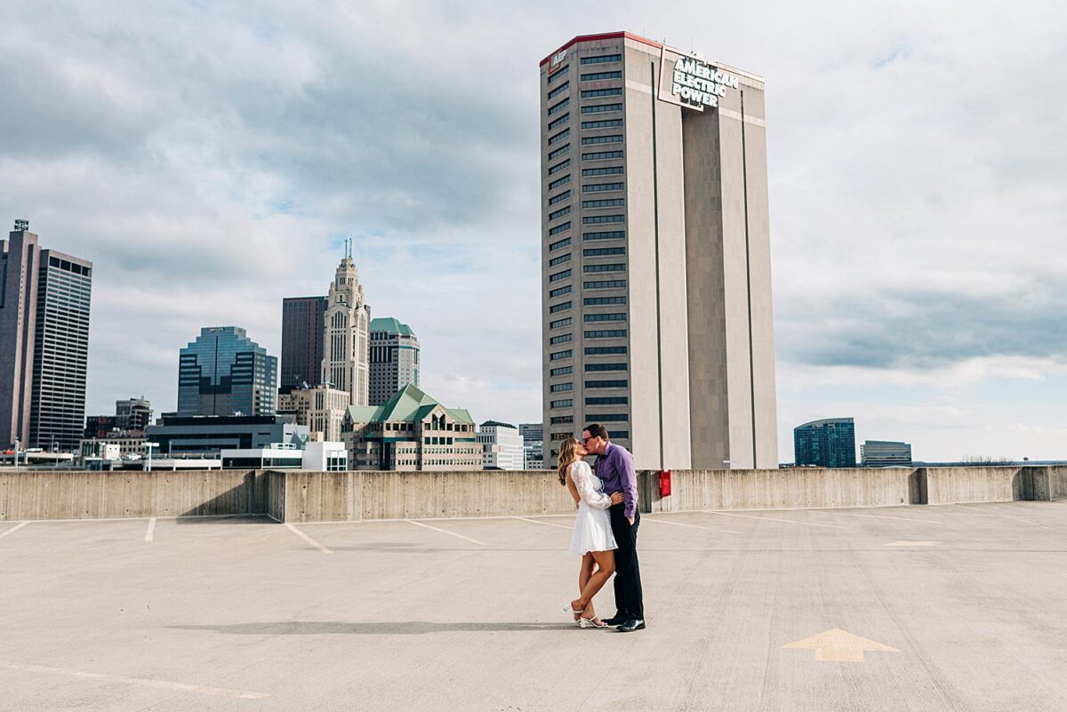Newly engaged couple embrace in a kiss on top of a parking garage in Downtown Columbus