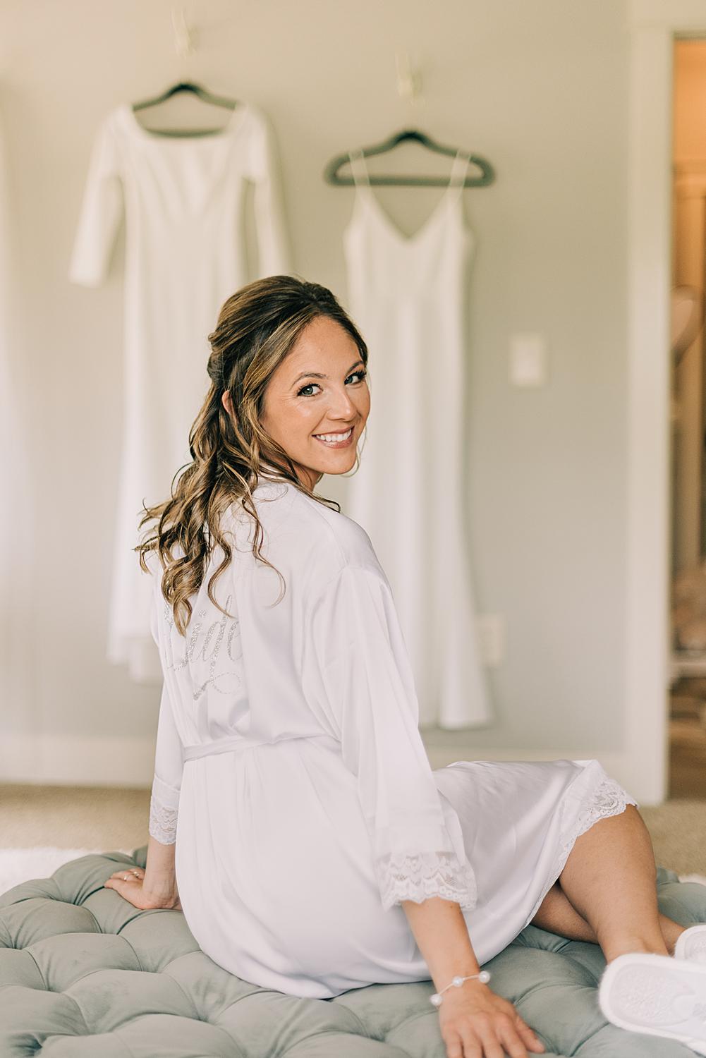 Bride poses for wedding photographers with her two wedding gowns hanging in the background