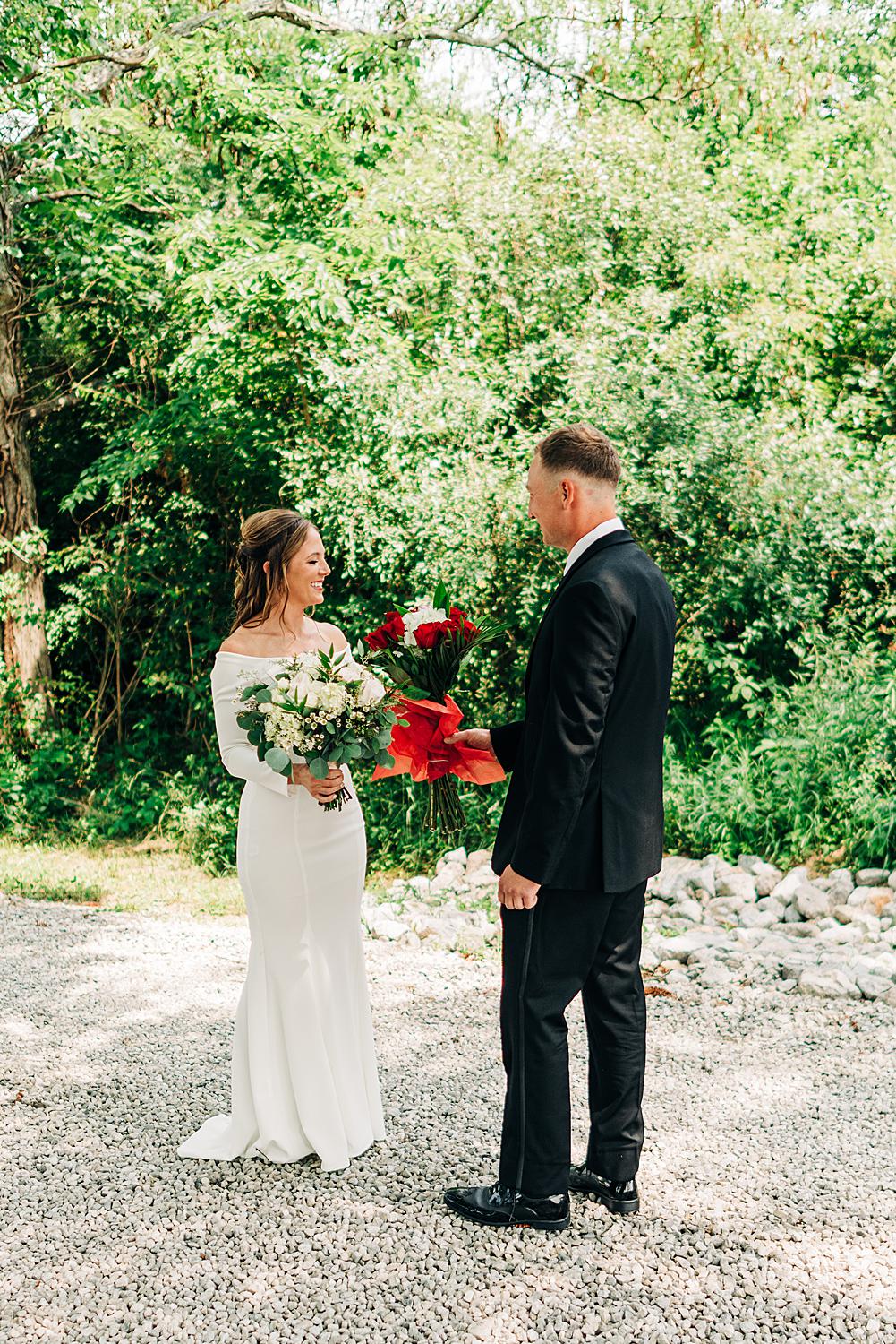 Groom hands his bride to be a bouquet of roses after their first look