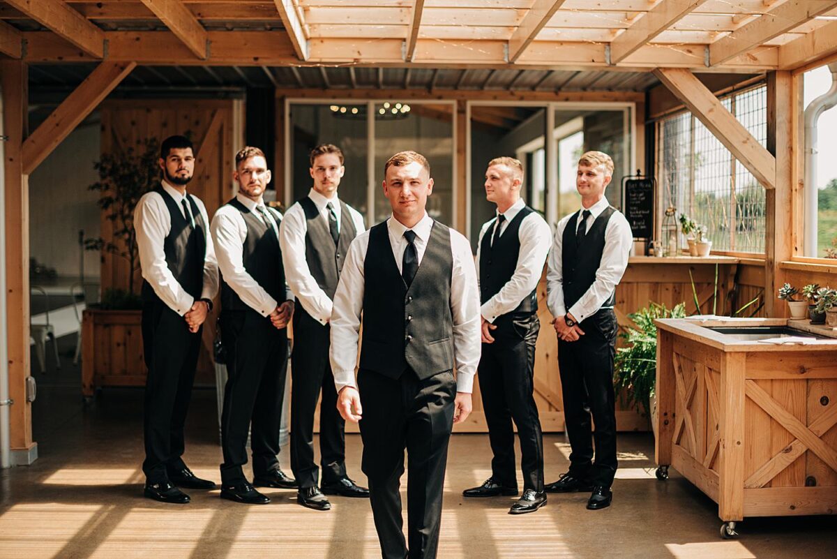 Groom walks towards wedding photographer during portraits with his groomsmen at Flora and Field wedding