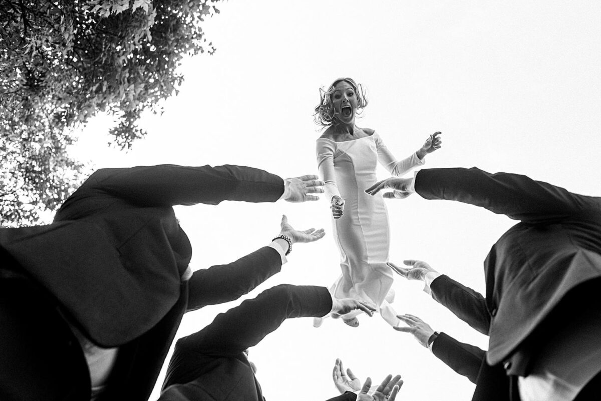 Worms eye view of Bride being tossed in the air by the groomsmen during wedding party portraits